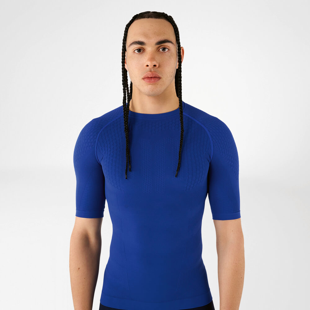 Een man draagt een blauw compressieshirt en kijkt zelfverzekerd naar de camera.