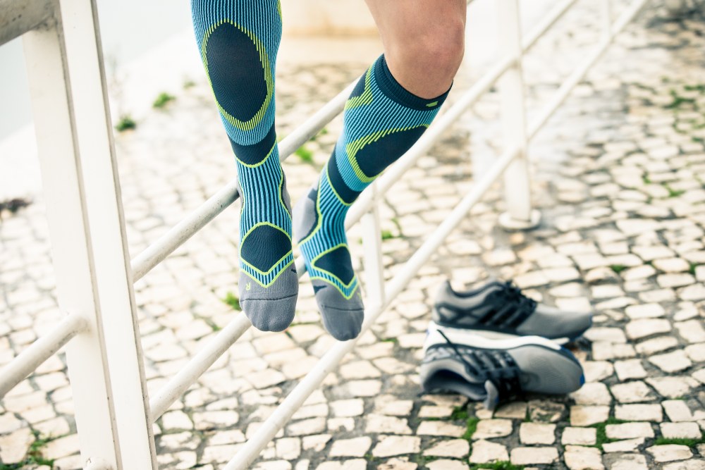 Man met blauwe en grijs lopende sokken zit op een hek en deed de schoenen uit