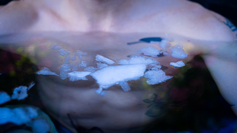 Bovenlichaam in ijsbad met ijsschotsen op het wateroppervlak Close-up van het bovenlichaam van een persoon tijdens ijsbaden, ijsschotsen drijven op het wateroppervlak voor de borst.