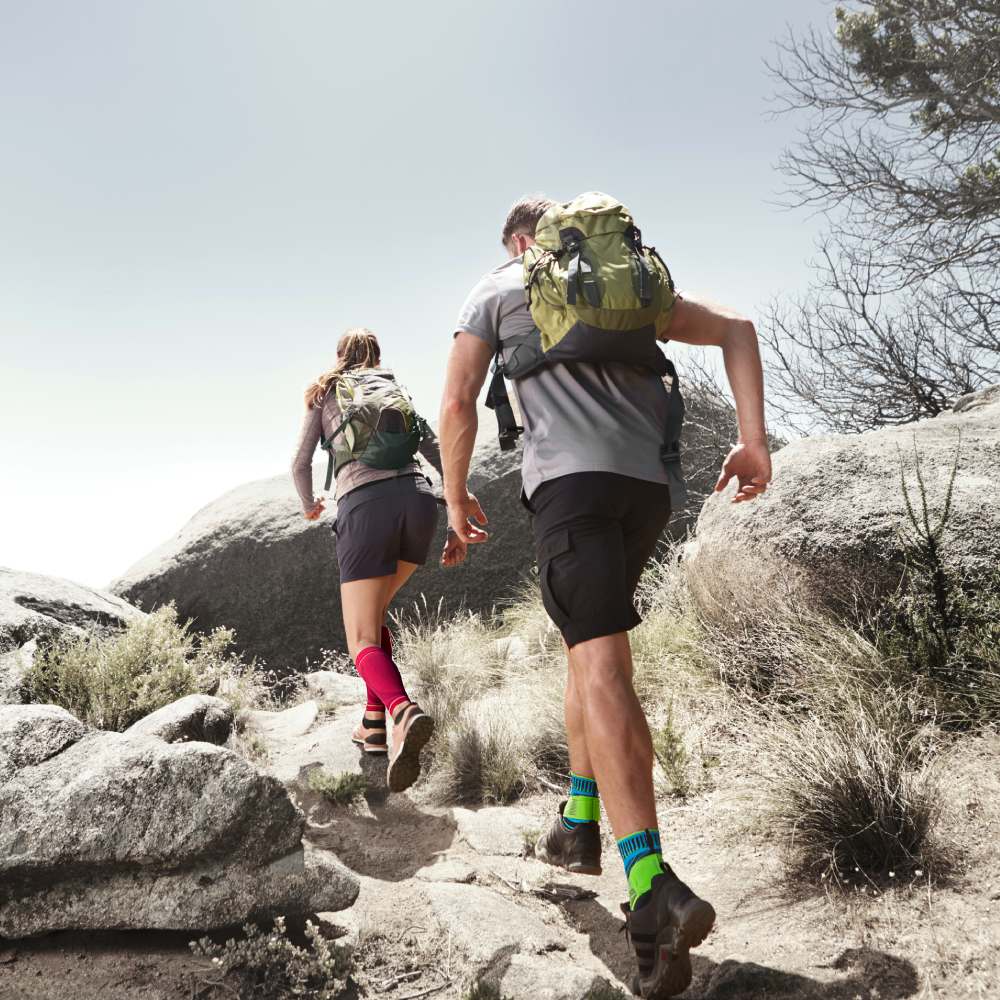 Krijg ondersteuning voor uw wandeltocht: bijvoorbeeld onze compressiemouwen en enkelondersteuning Pärchen met roze calfollaves en blauwe enkelbanden in de zomer dwaalt een kleine klim omhoog tussen rotsen