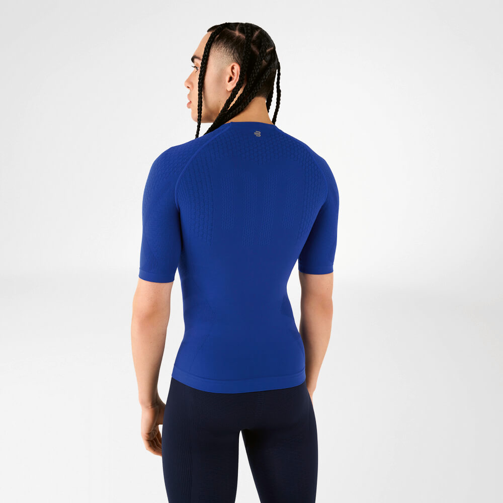 Een man draagt een blauw compressieshirt, staat met zijn rug naar de camera en kijkt over zijn schouder.