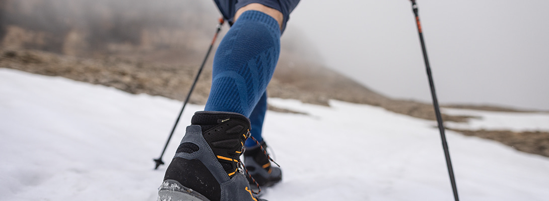 Merino Hiking Socks Light Blue tijdens het wandelen Persoon wandelt via met sneeuw bedekte rotsen. Ze draagt Merino -wandelsokken