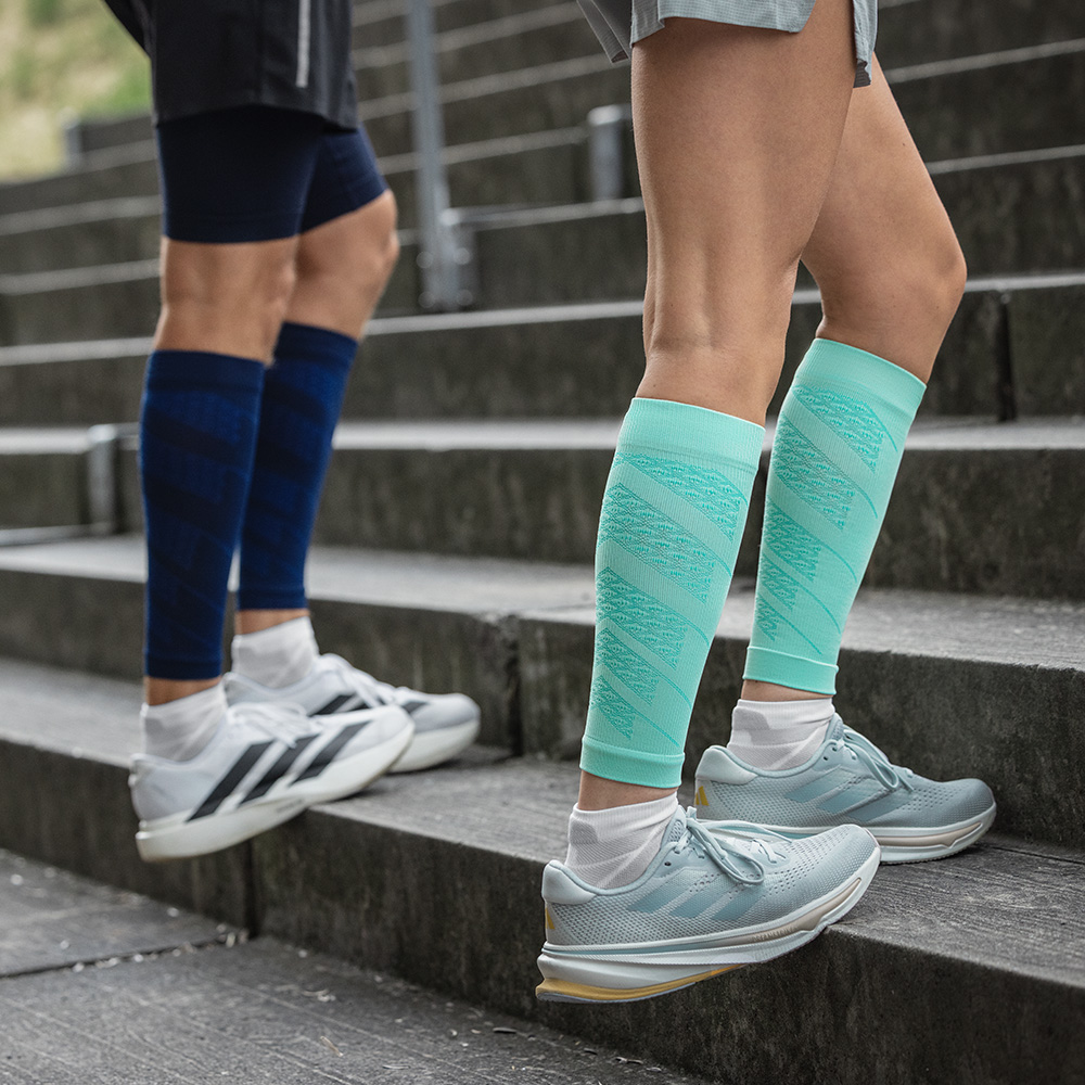 Twee hardlopers tijdens traptraining buiten. Ze dragen Run Performance Sleeves met compressie in mint en navy, die zorgen voor stabiliteit en een betere doorbloeding.