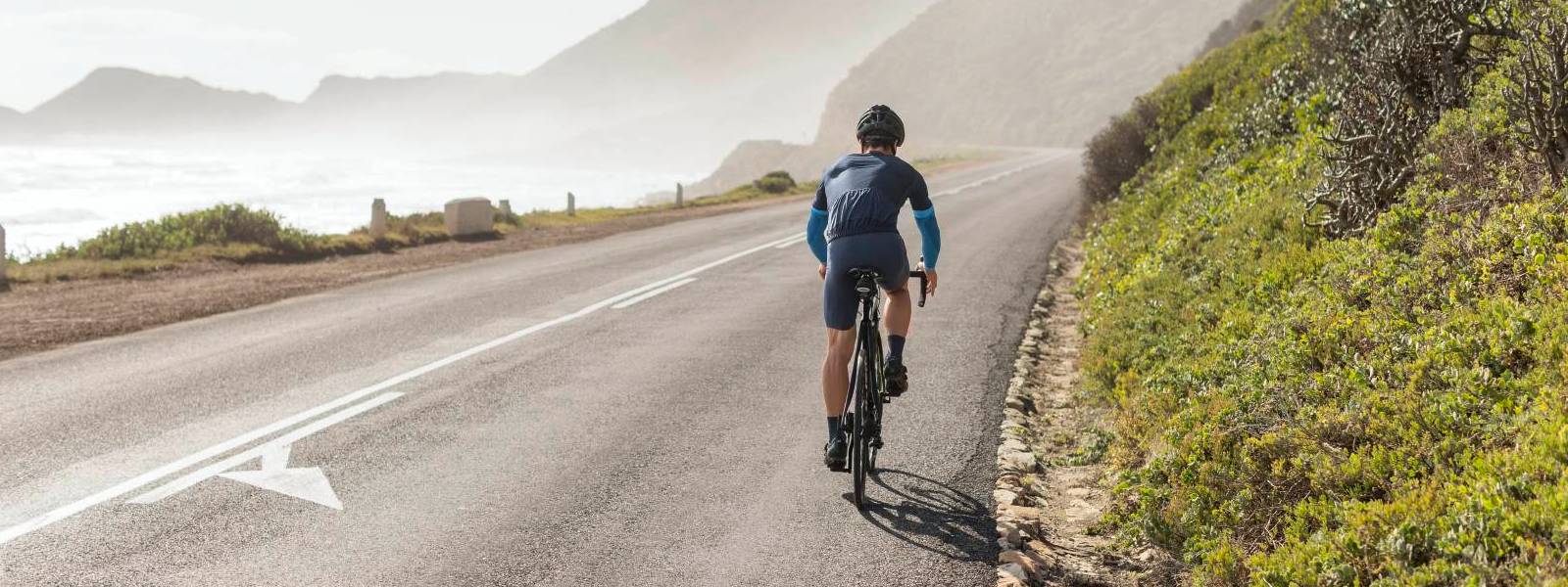 ARM MOEVEN RIJD Fiets Fietsers dragen blauwe armmouwen en rijdt op een straat op de helling met een uitzicht op zee