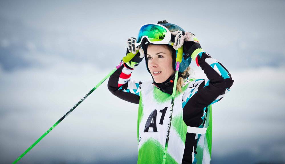 Skir-racer Andrea Limbacher in een blauw en wit zwart racepak spreekt haar skiglazen aan met de stokken in haar handen