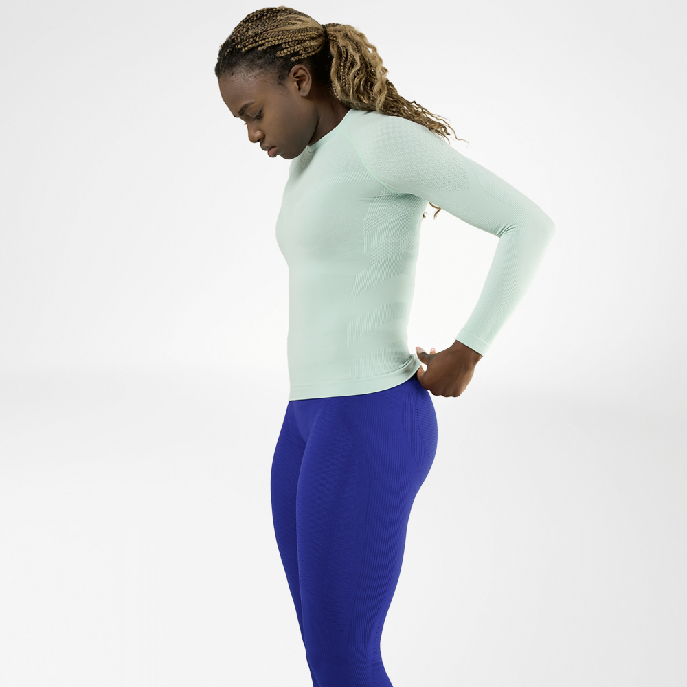 Vrouw in een mintgroen langmouwshirt en blauwe compressiebroek, zijaanzicht