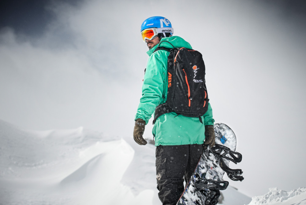 Snowboarders met een groen jasje en bord in de hand kijkt naar zijn schouder naar achteren