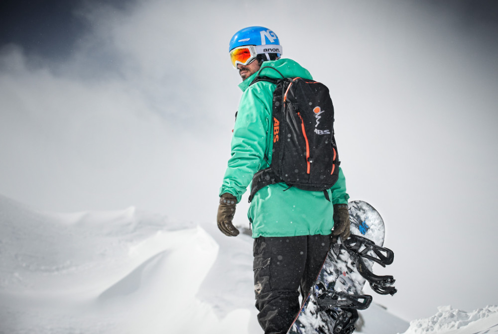 Welke krachtige dijen doen snowboarden? Hoe versterk ik mijn rug? We hebben een paar tips Snowboarders met een groen jasje en bord in de hand kijkt naar zijn schouder naar achteren