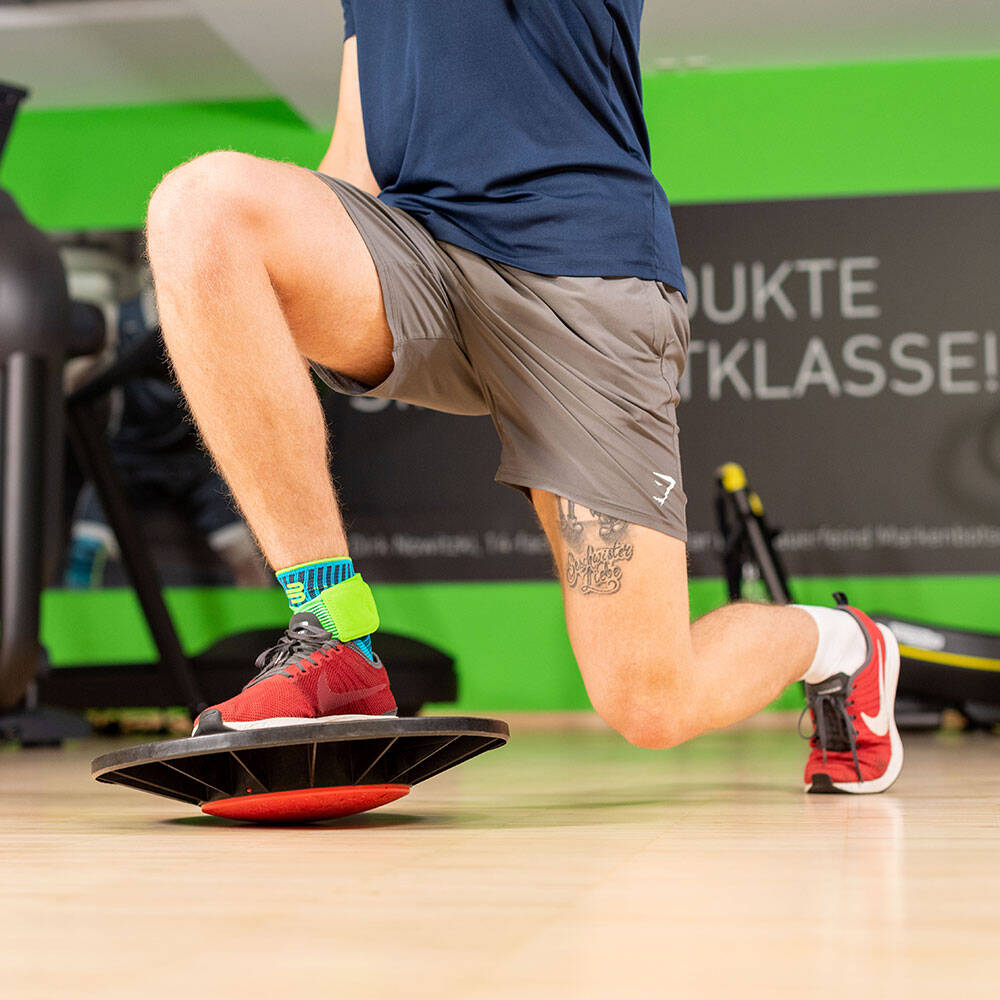 De man in een sportschool maakt een long met het voorpoot dat op een balanskussen staat en een enkelverband draagt