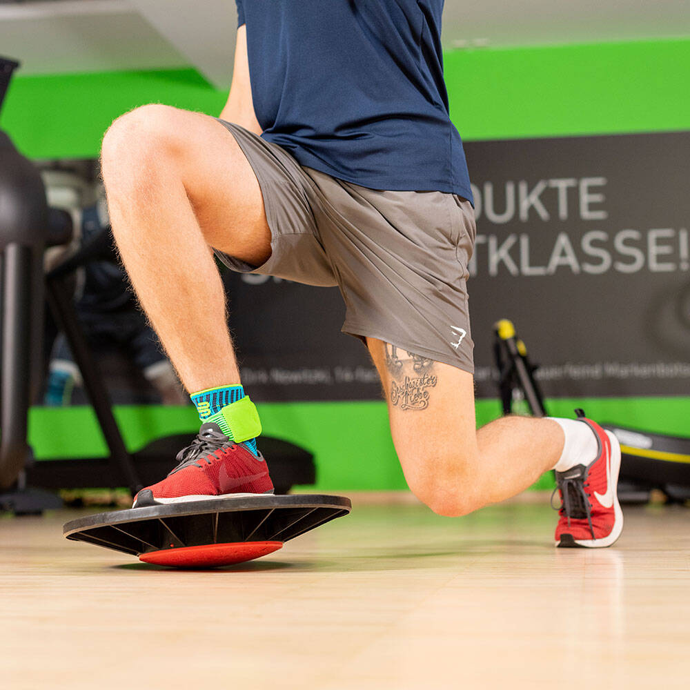 Lunges kunnen worden uitgebreid met een balanspad naar een complexe stabilisatieoefening De man in een sportschool maakt een long met het voorpoot dat op een balanskussen staat en een enkelverband draagt