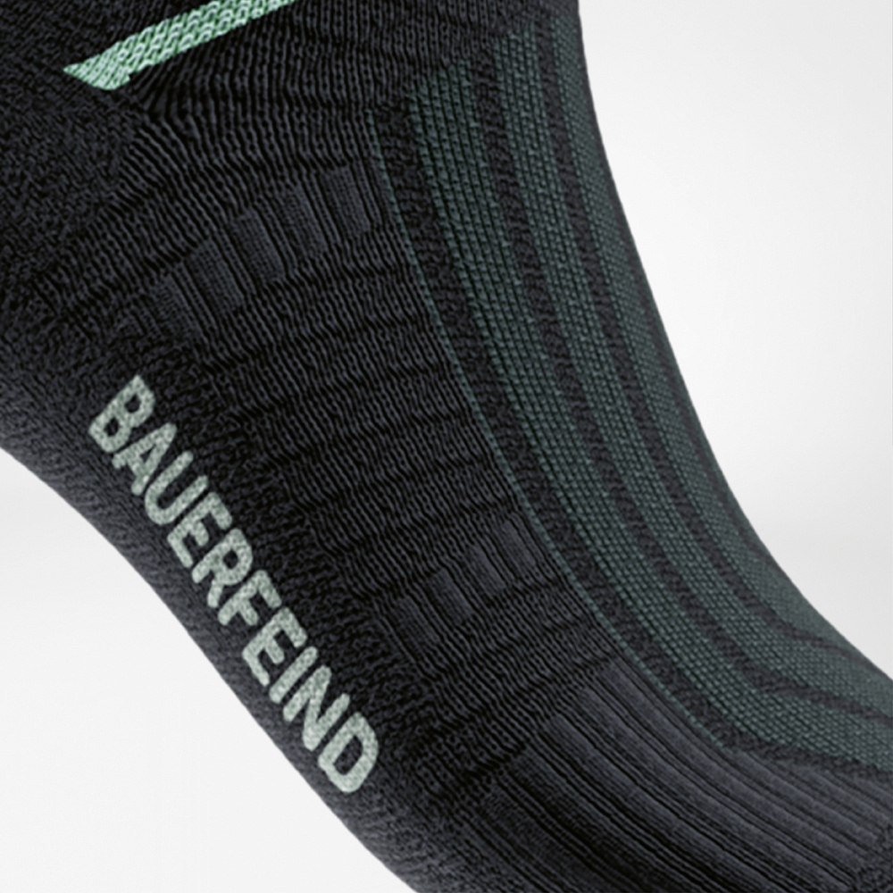 Detailweergave van de Run Performance Midcut Socks in zwart met een mintkleurig arch-liftelement. De close-up benadrukt de speciale compressiezone bij de voetboog voor stabiliteit en ondersteuning.