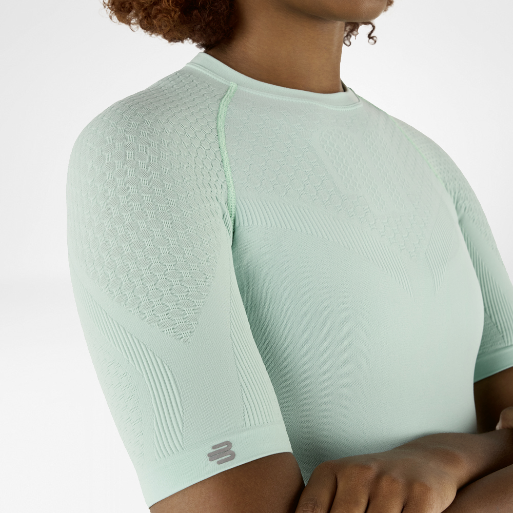 Zijdelingse close-up van een mintgroen compressieshirt met gedetailleerde getextureerde stof op de schouder en arm.