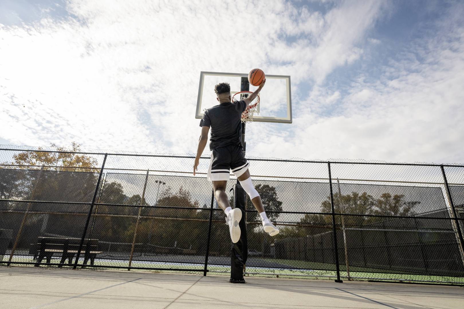 Basketbalspelers met een witte knieband tijdens het dunkeren op een straatbalveld