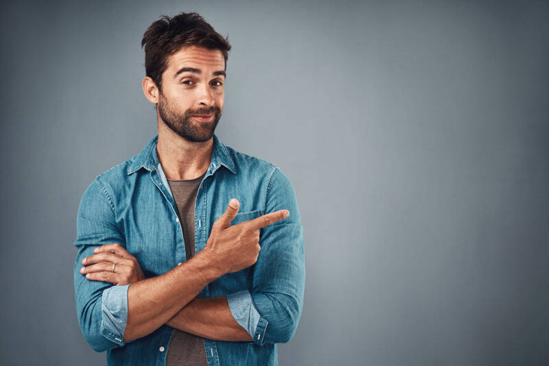 Glimlachende man in een denim shirt toont met zijn wijsvinger aan de zijkant