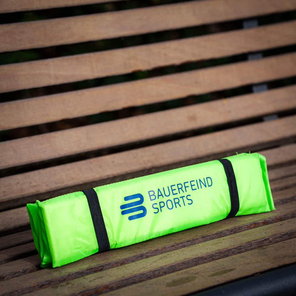 Handig zitkussen voor onderweg Opgevouwen Bauerfeind Sports zitkussen in felgroen, veilig opgeborgen op een houten bank.