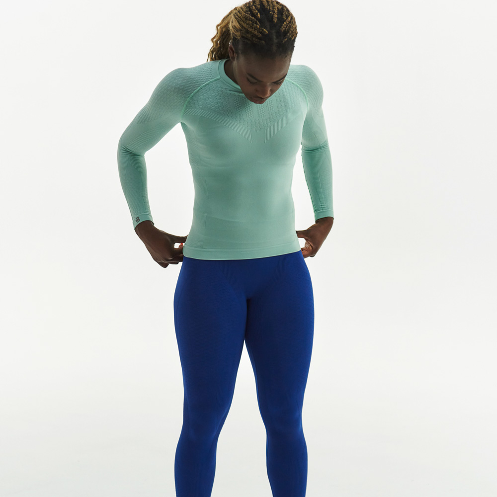 De nieuwe set compressiekleding voor vrouwen Vrouw in mintgroene compressietop en donkerblauwe compressiebroek kijkt naar de vloer en heeft haar handen op haar heupen