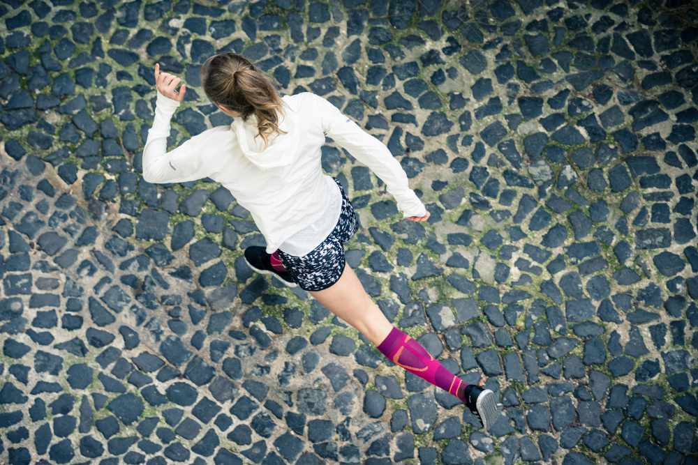 Bird's Eye View: Runner in een wit hardloopjasje en met roze hardloopsokken loopt over een Old Town Street