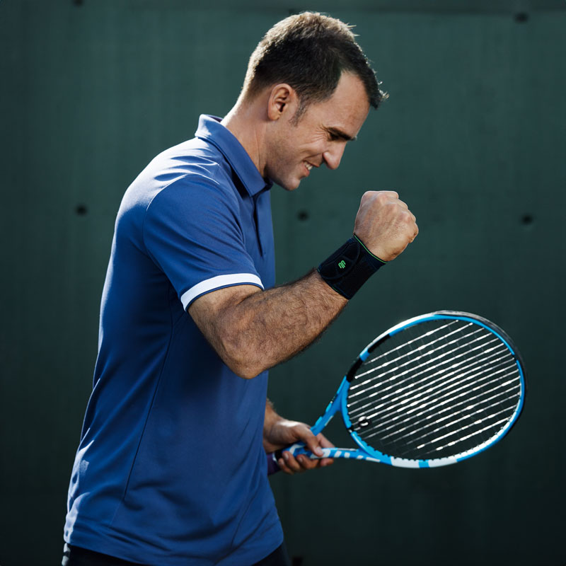 Tennisspeler met een zwarte polsbandje heft zijn vrije arm op en klontert de vuist tevreden