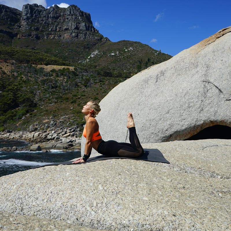 Vrouw bij de outdoor yoga in de Königskobra -pose heeft haar handen ondersteund en haar voeten verticaal naar boven gestrekt