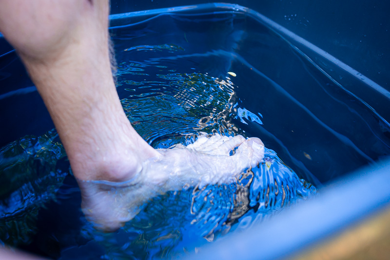 Eerste contact: De voet waagt zich in het ijskoude water! Een voet dompelt zich onder in koud water in een blauwe bak. Het heldere water vertoont lichte rimpelingen en lichtreflecties op het oppervlak.