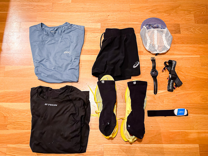 Hardloopkleding en -uitrusting voor halve marathon - Voorbereiding voor de racedag Voorbereidingen voor de halve marathon: Een volledige race-outfit, inclusief blauwe hardloopkleding, gele hardloopschoenen en technische accessoires zoals een hartslagmonitor en een hardloophorloge, ligt klaar.