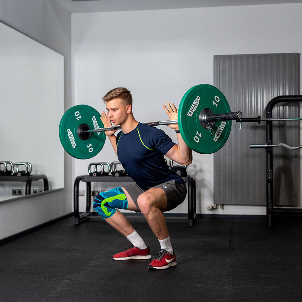 Man in de sportschool met een kniestand maakt een squat met een barbell op de achterkant