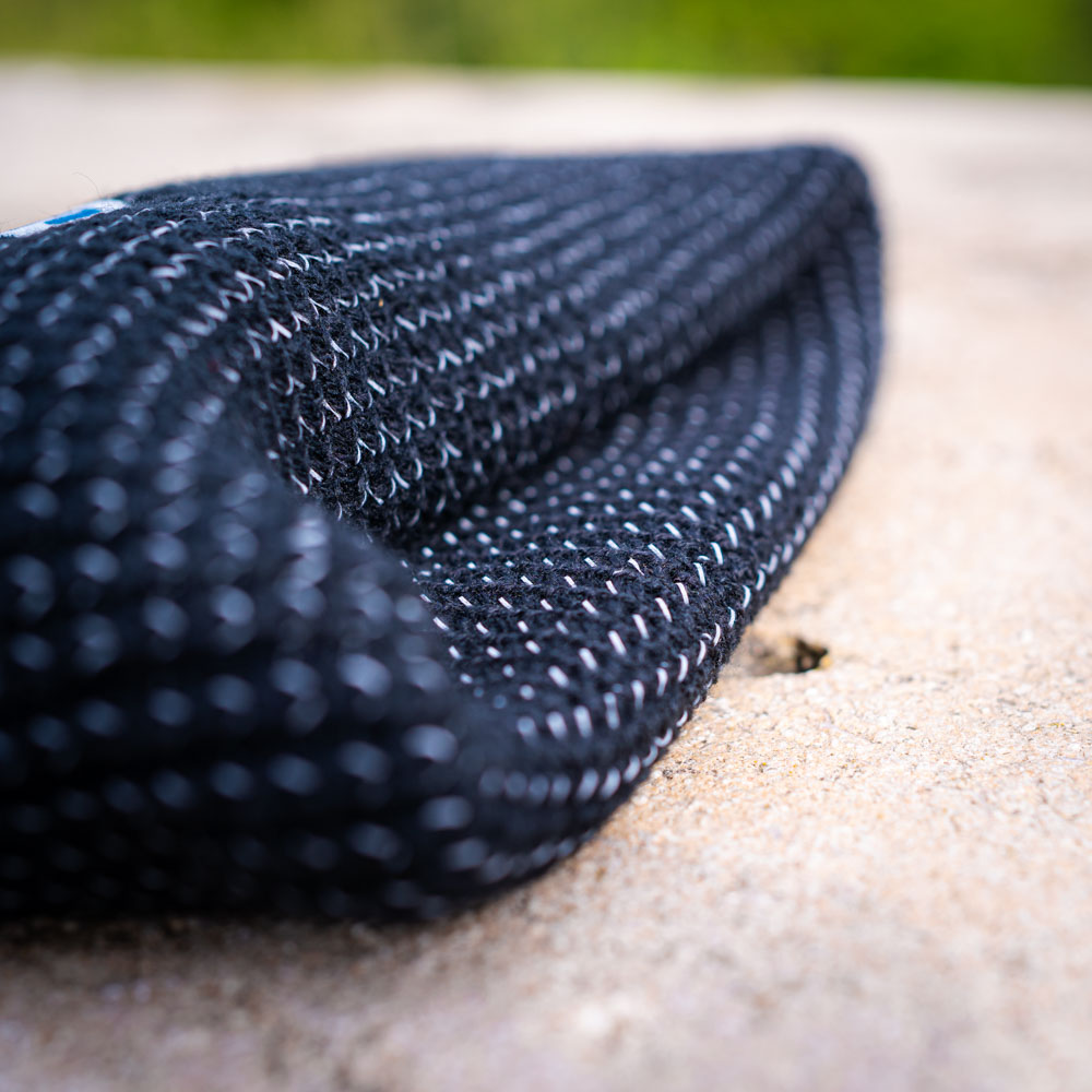 Duurzaam en warm: De Bauerfeind Sports muts voor buitenavonturen Een gevouwen zwarte Bauerfeind Sports muts op een steen, met de grove textuur duidelijk zichtbaar.