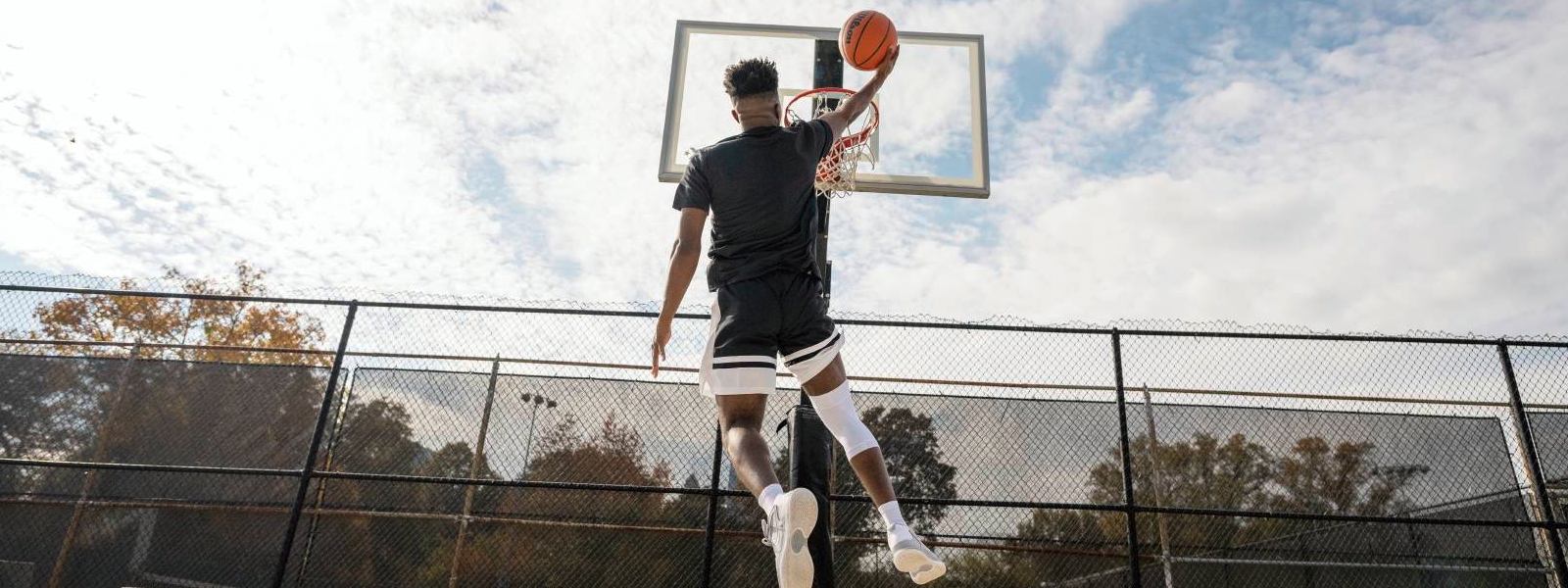 Basketbalspeler springt op een vrije ruimte naar de mand en draagt ​​een witte knieband