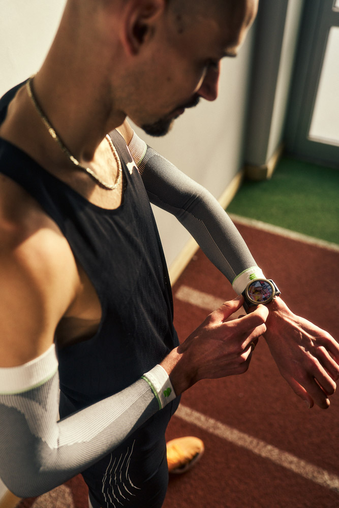 Hendrik Pfeiffer kijkt tijdens een indoor training naar zijn sporthorloge, met compressie arm sleeves voor extra stabiliteit en prestaties.