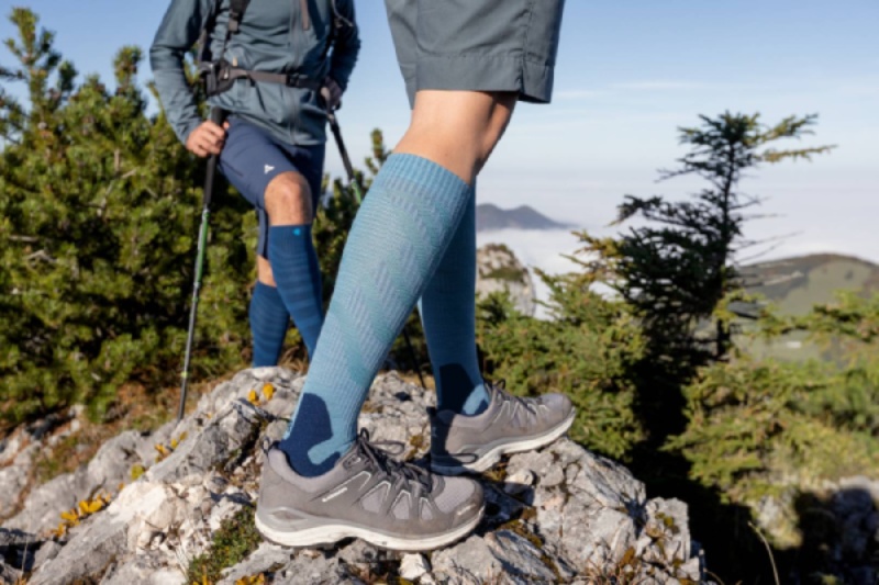 Twee wandelaars met Outdoor Merino Compression Socks op een rotsachtig pad. Deze compressiesokken bieden optimaal comfort en ondersteuning voor lange wandelingen in een natuurlijke omgeving.