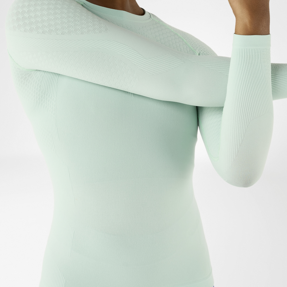 Close-up van een sportieve man in een lichtgroen, langmouwig compressieshirt die zich uitrekt.