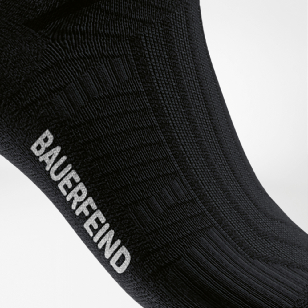 Ondersteuning van de voetboog en ribbelstructuur bij de zwarte Run Performance Sock Zijaanzicht van een zwarte sportsok met ribbelstructuur rond de middenvoet en wit “BAUERFEIND”-logo – voor extra ondersteuning van de voetboog tijdens het lopen.
