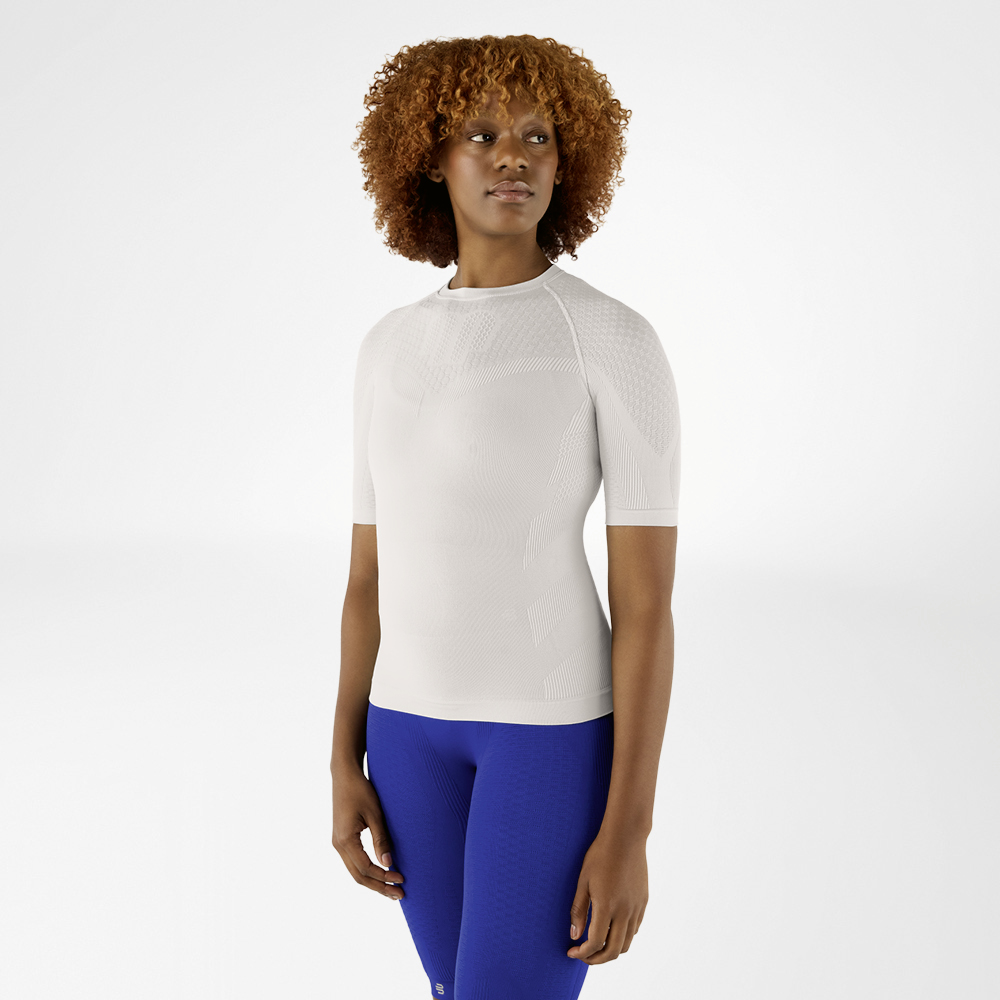 Zilvergrijs Compressieshirt en Blauwe Leggings Vrouw met krullend haar in een zilvergrijs compressieshirt en blauwe leggings. Ze staat naar voren gericht en kijkt opzij.