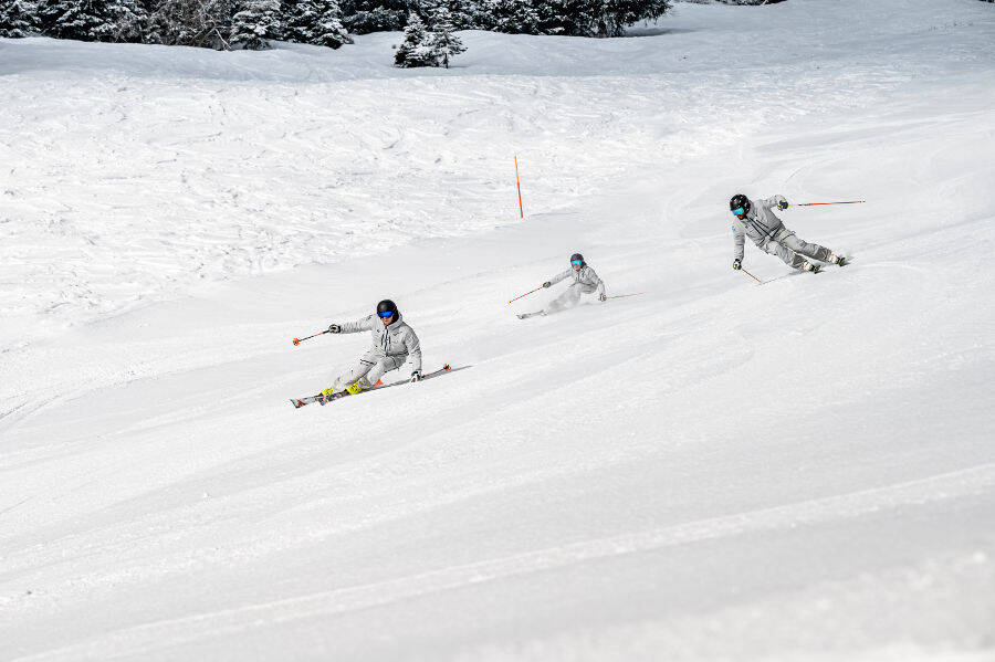 Drie in één grap: ga gewoon op een wintervakantie met je vrienden Drie skiërs gekleed in grijs grijs aan de zijkant van een gezamenlijke afdaling en in hellende rijposities.
