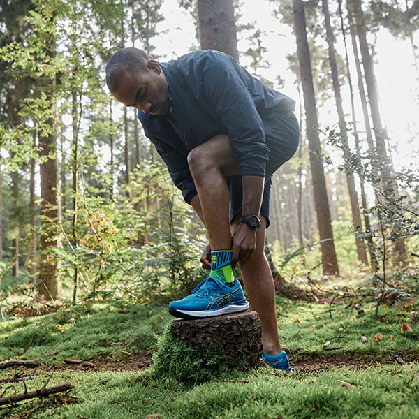Hardloper in het bos maakt zijn verband in orde Een hardloper staat in een dicht bos en maakt zijn enkelverband in orde