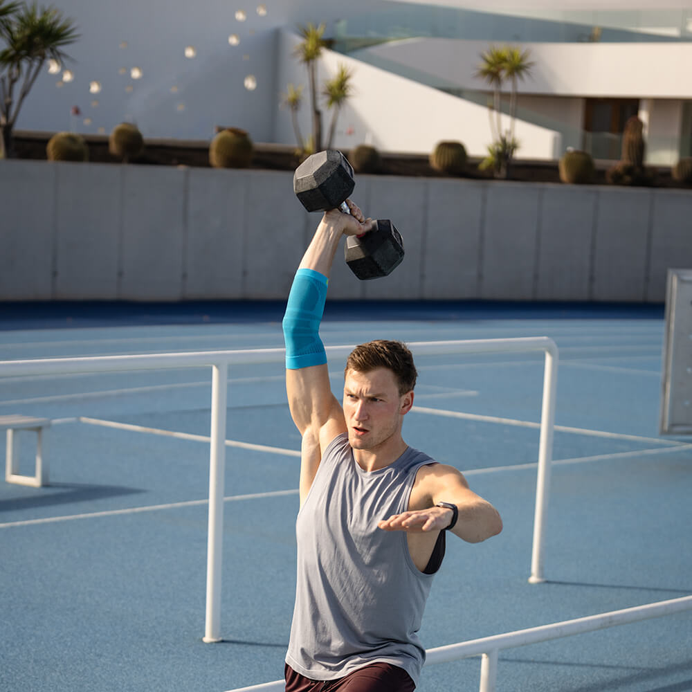 Ellenbogenensleeve tijdens de training De man traint met een halter en draagt een sportvleeve voor de elleboog