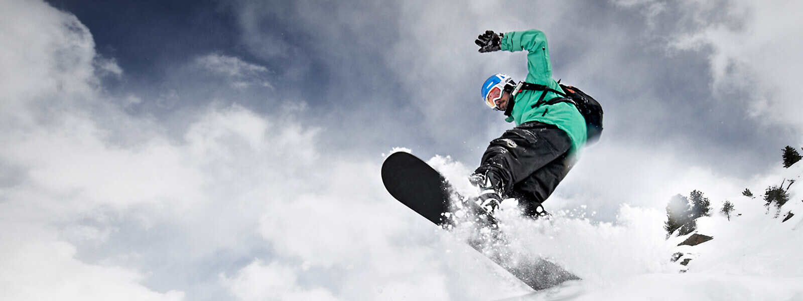 Al het groen komt van boven: een snowboarder springt over een top Kikkerperspectief: snowboarders in een groene jas komen van boven boven een kuif bord en veel gefluisterde sneeuw is te zien