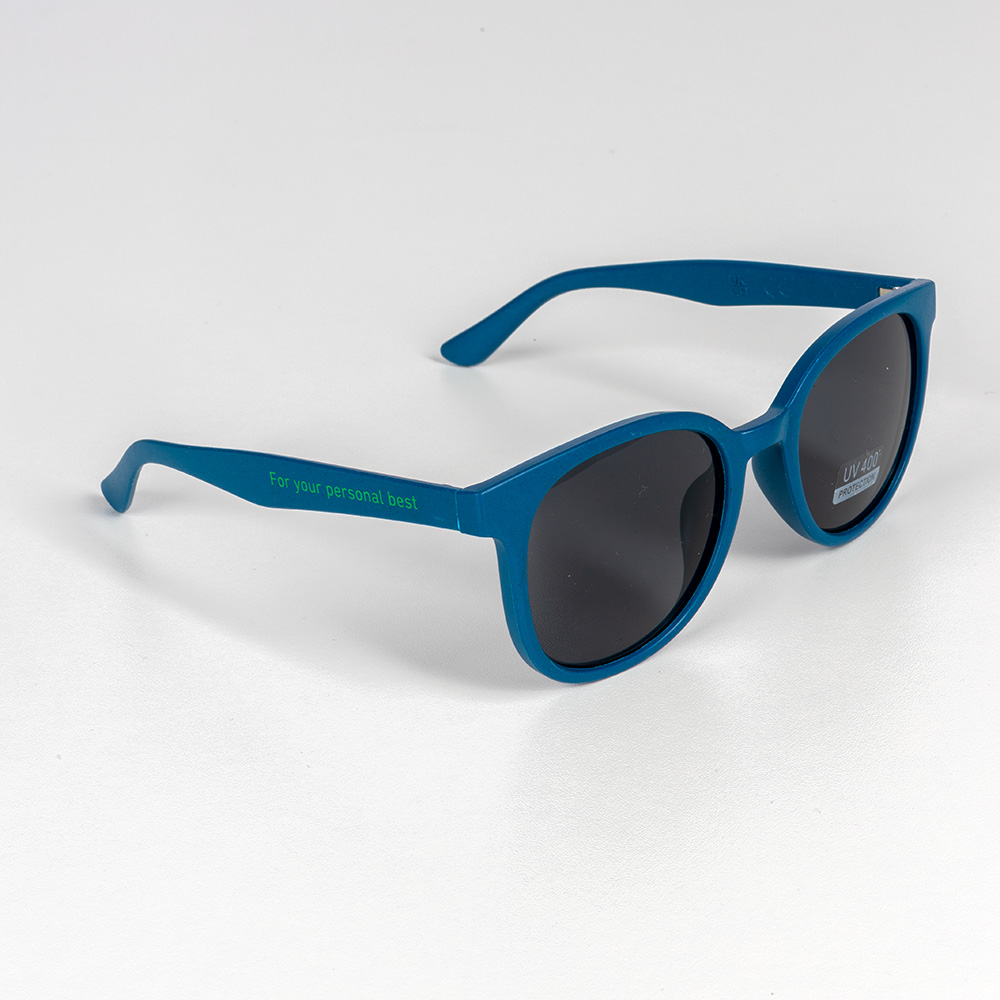 Klaar voor elke zonnestraal – met focus en stijl. Blauwgroene zonnebril met donkere glazen en de slogan „For your personal best“ op de poot. De bril ligt op een witte ondergrond.