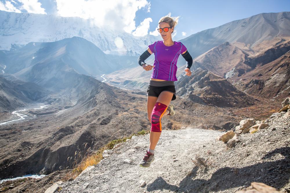 Vrouw rent door een hoog berglandschap en draagt ​​een roze kneege