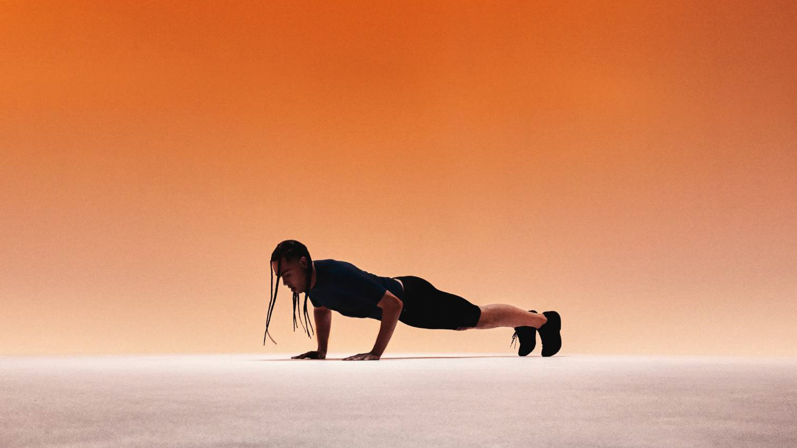 Atleet in blauwe sportkleding met compressieshirt en compressiebroek die push-ups doet voor een oranje achtergrond.