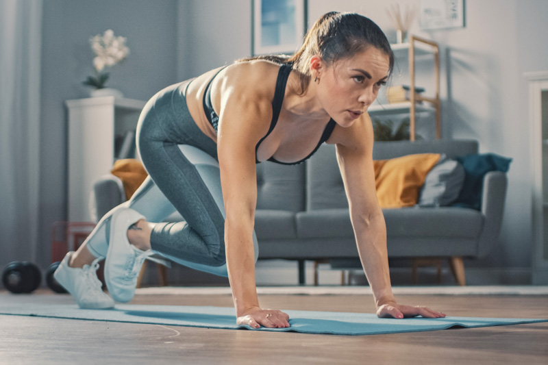 Krachttraining voor hardlopers: een paar minuten ertussenin zijn voldoende Vrouw maakt bergbeklimmers in de woonkamer op de achtergrond een bank en planken