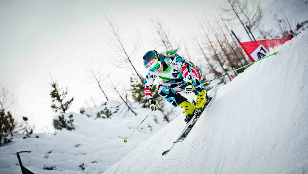 Ski-loper in een blauw en wit-zwart racepak drijft op de achtergrond een steile as op de achtergrond naar beneden Een rode poort is te zien