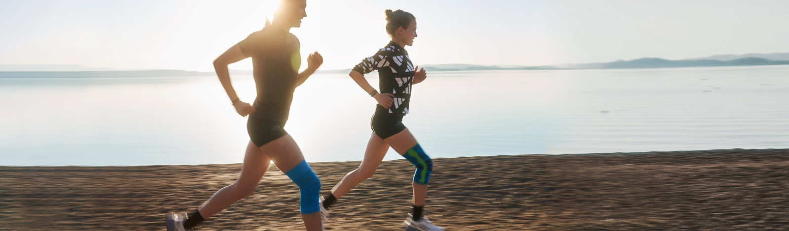 Met een knie van een hardloper kan een knieband de situatie effectief verhelpen Twee lopers met kniebanden lopen op een strand naast een meer bij schemering
