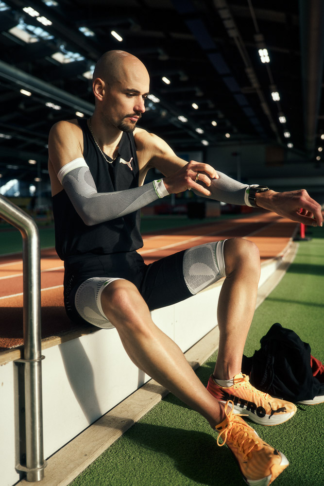 Marathonloper Hendrik Pfeiffer zit aan de rand van een indoorbaan en trekt compressie arm sleeves aan ter voorbereiding op zijn training.