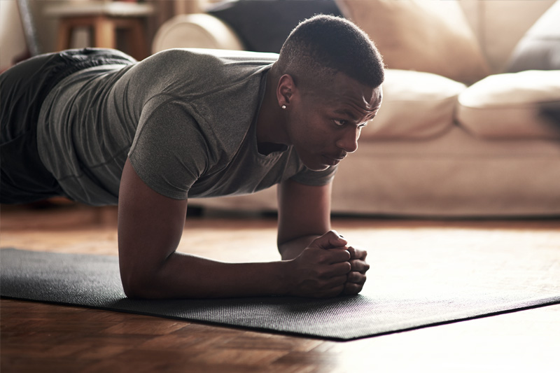 Krachttraining voor hardlopers: de plank als een woonkameroefening voor de televisie De mens maakt een lichte bank in de woonkamer in de woonkamer op de achtergrond