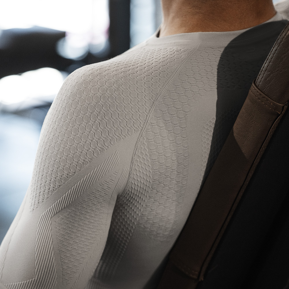 Maximale support bij elke beweging – Jouw trainingsshirt met compressie Close-up van de rechterschouder van een man in een strak beige compressieshirt met functionele zones voor gerichte spierondersteuning en maximale bewegingsvrijheid, vastgelegd in een sportieve setting.