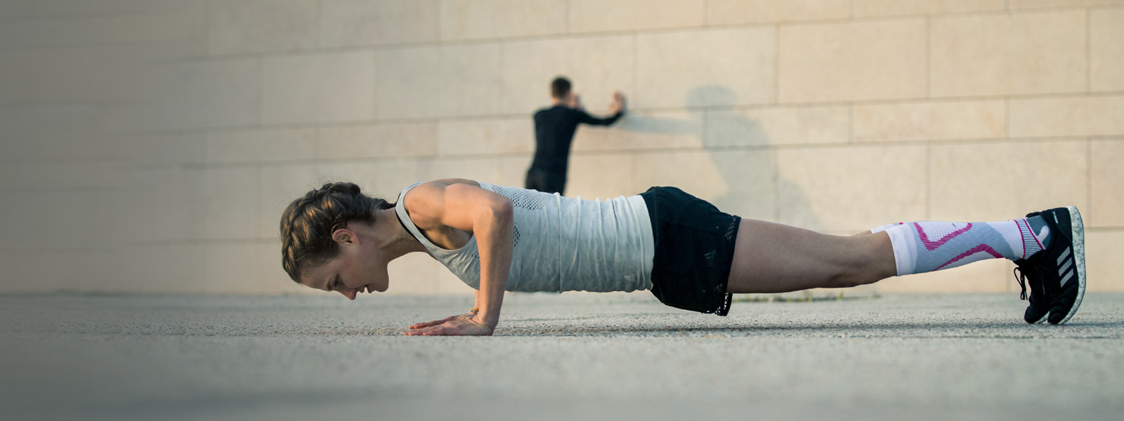 Vrouw maakt push-ups op een betonnen vloer op de achtergrond die een man uitstrekt op een muur