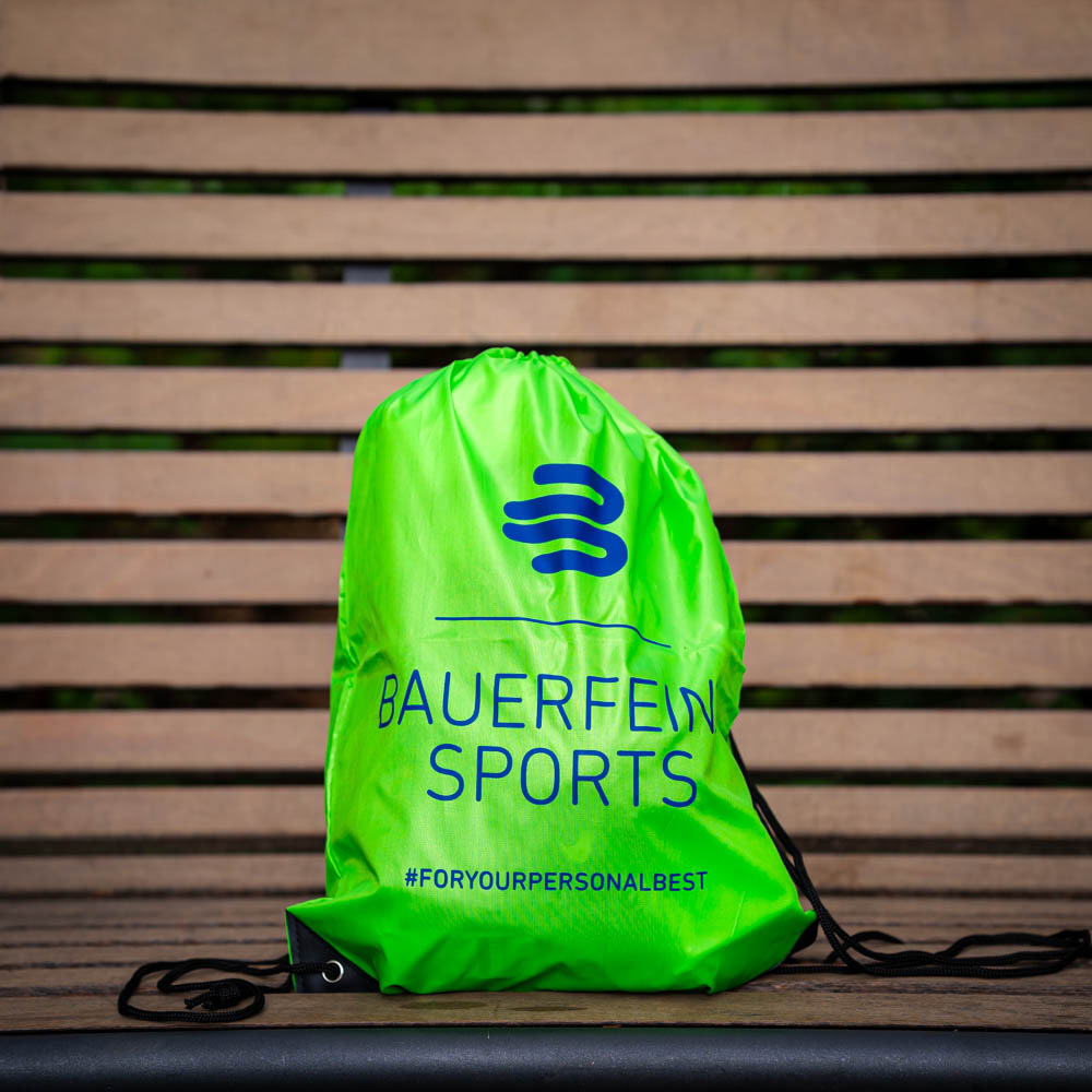 Praktisch en stijlvol: De Bauerfeind Sports gymtas voor jouw doelen Een groene Bauerfeind Sports gymtas ligt op een houten bank, met het logo en de hashtag #foryourpersonalbest zichtbaar.