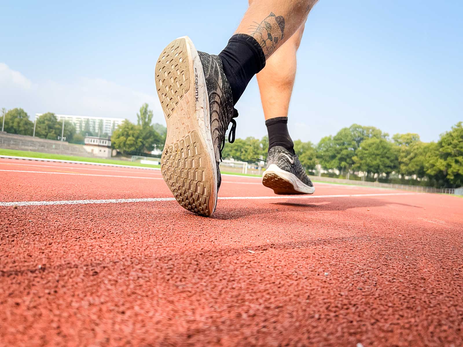 Hardlooptraining op de Renbaan – Focus op Vastberadenheid en Sportieve Doelen. Close-up van de schoenen van een loper op de rode renbaan, klaar voor training. De scène symboliseert vastberadenheid en sportieve doelen.