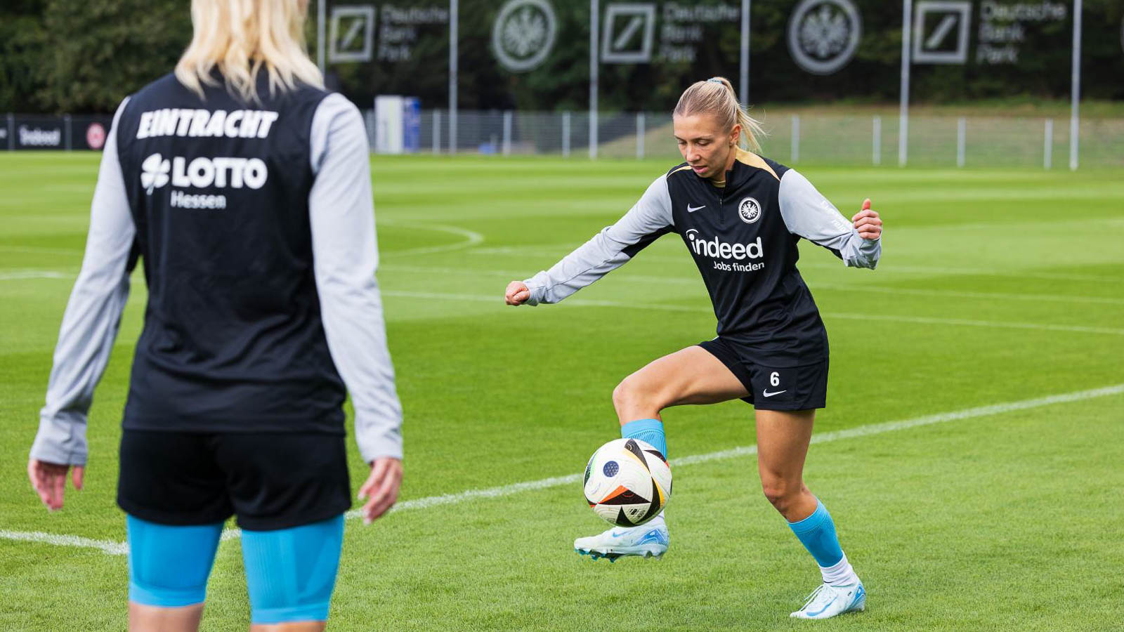 Balcontrole en Techniektraining bij Eintracht Frankfurt Eintracht-Frankfurt-speelster in actie terwijl ze de bal beheerst. Een ander teamlid kijkt naar de training op de achtergrond. Focus op techniek en precisie.